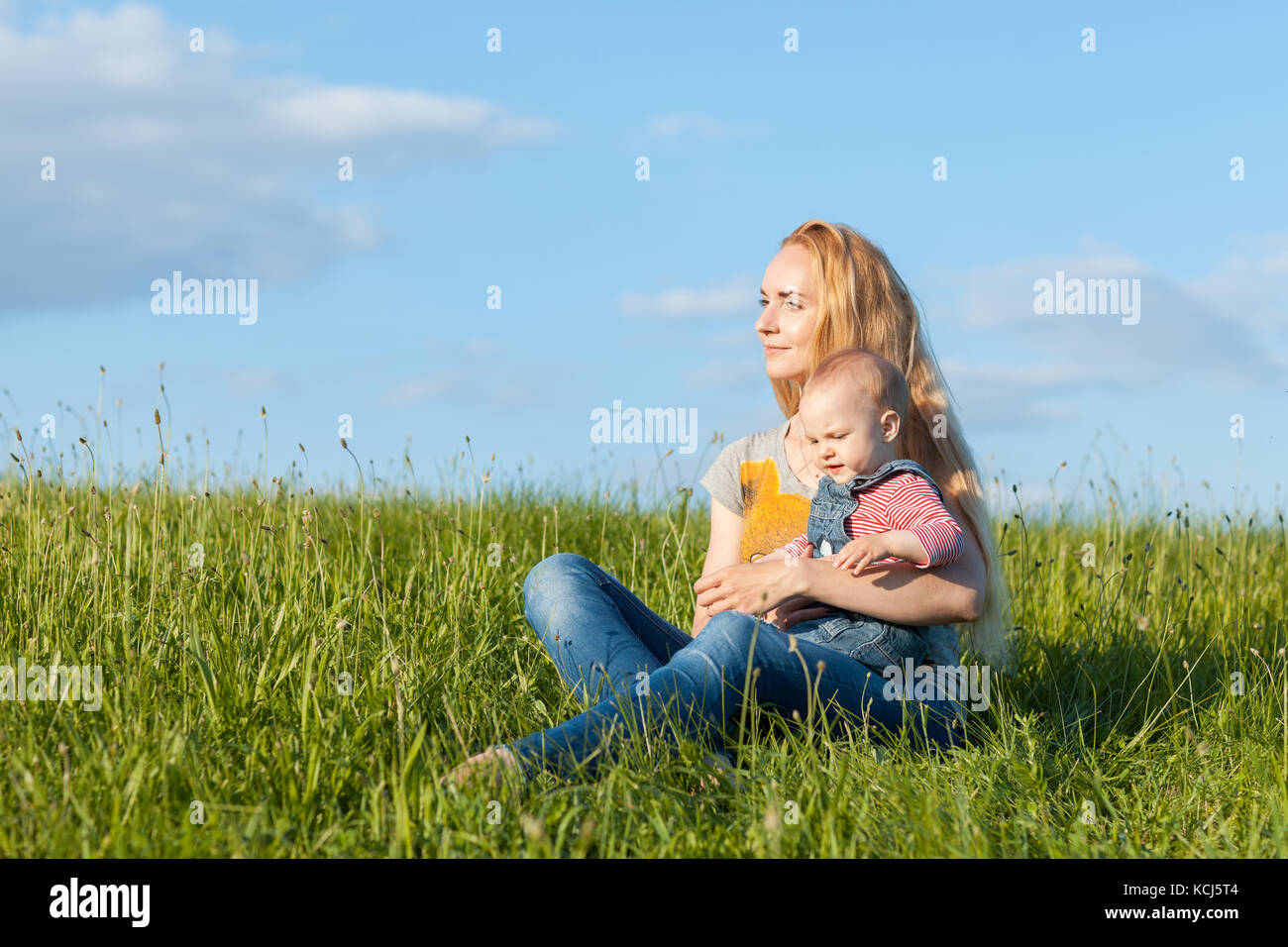 Jeune mère assise dans l'herbe et tenant un enfant Banque D'Images