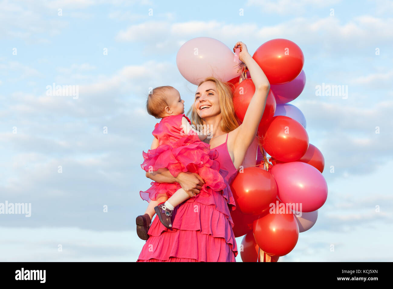 Mère et fille en rose robes. maman est titulaire d'une fille et un tas de ballons dans ses bras Banque D'Images