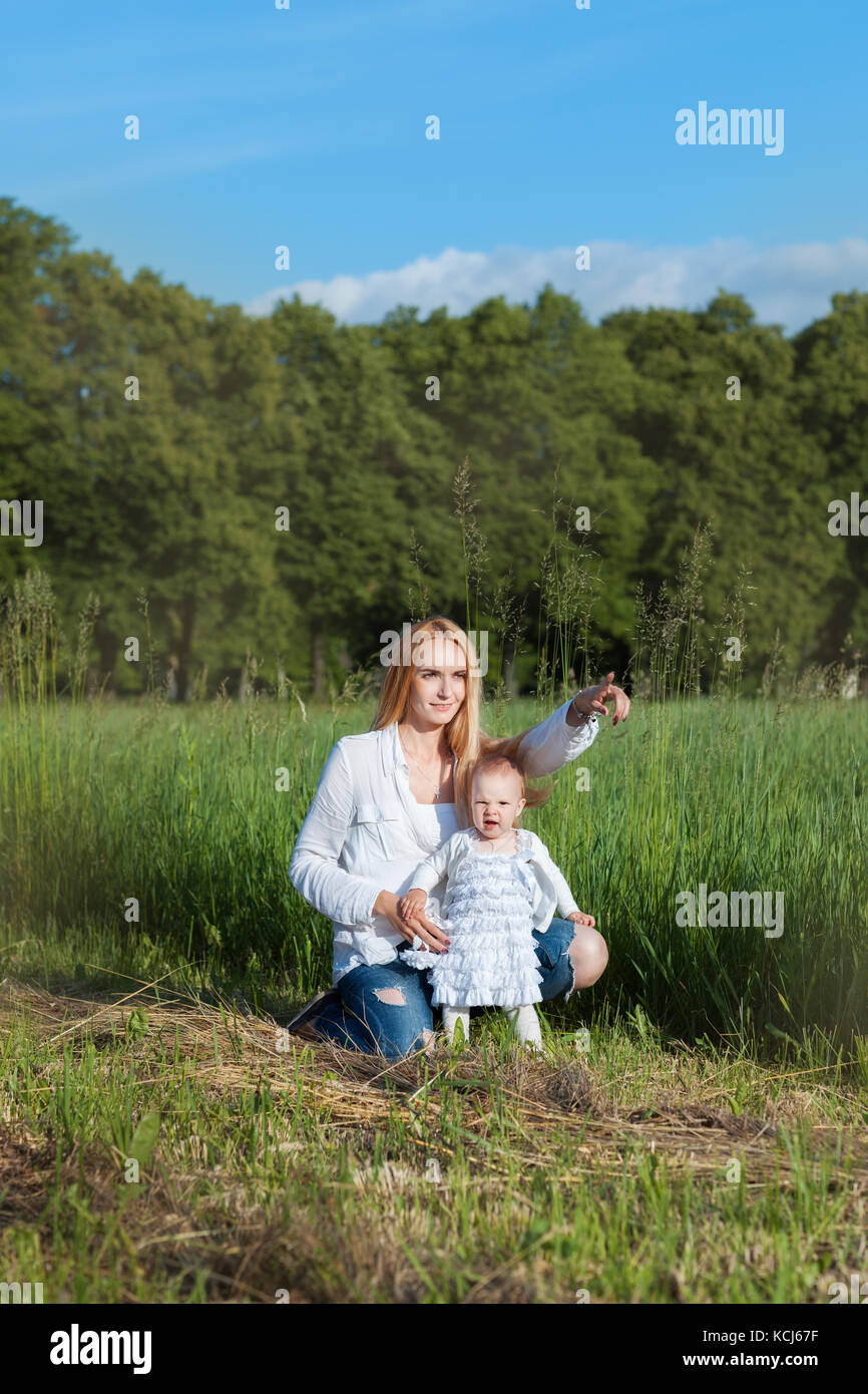 Jeune maman avec sa petite fille dans un champ. maman montre sa main en avant Banque D'Images