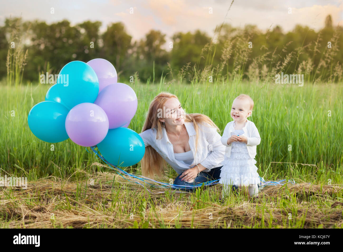 Jeune mère et sa fille assise sur l'herbe. maman détient balloons Banque D'Images