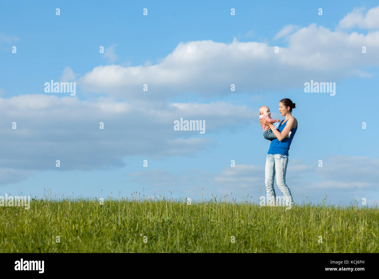 Jeune maman avec sa fille sur un pré vert contre le ciel avec des nuages Banque D'Images