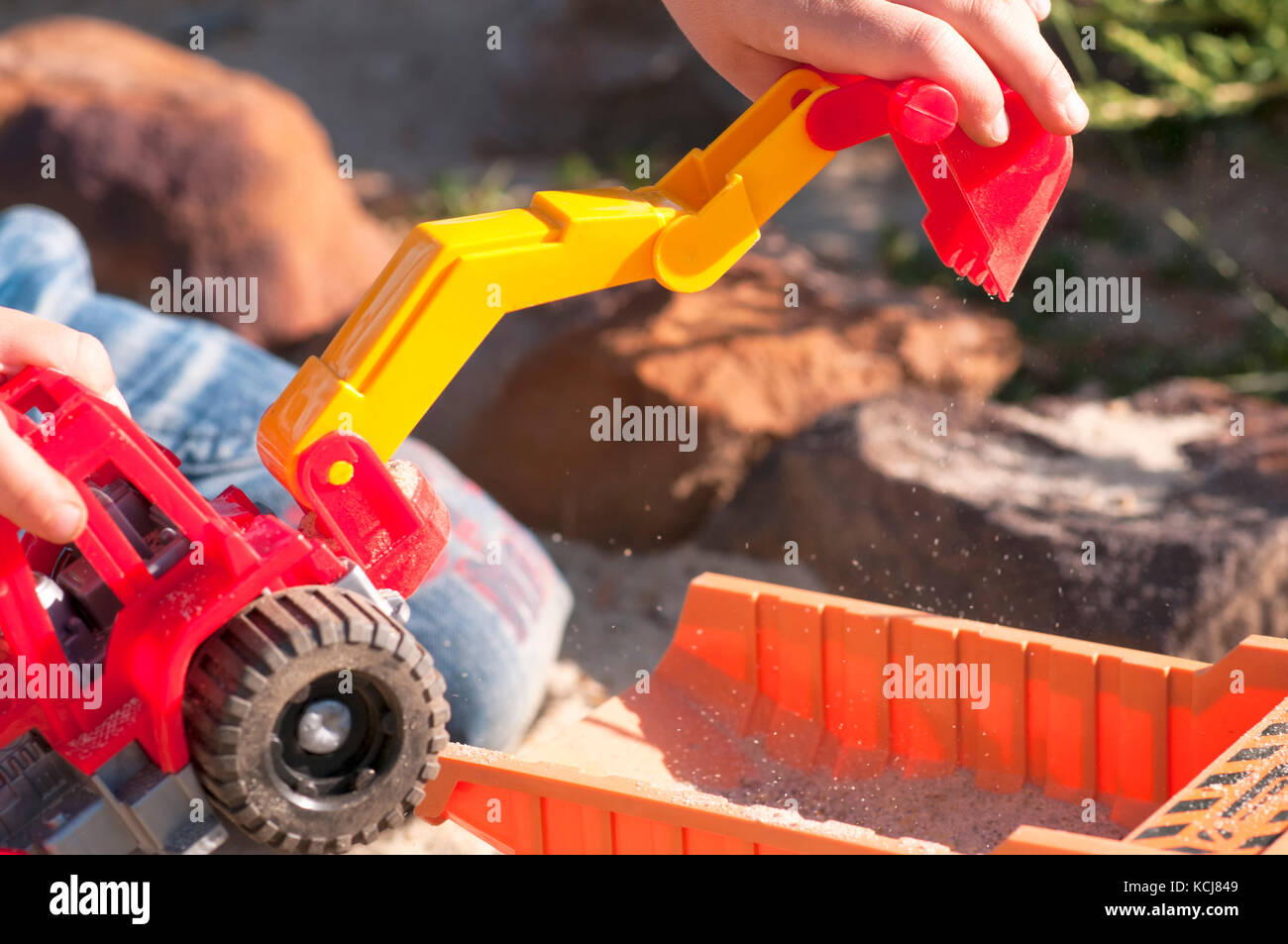 Un enfant joue dans le sable avec de grandes voitures de jouet, une pelle, un camion Banque D'Images