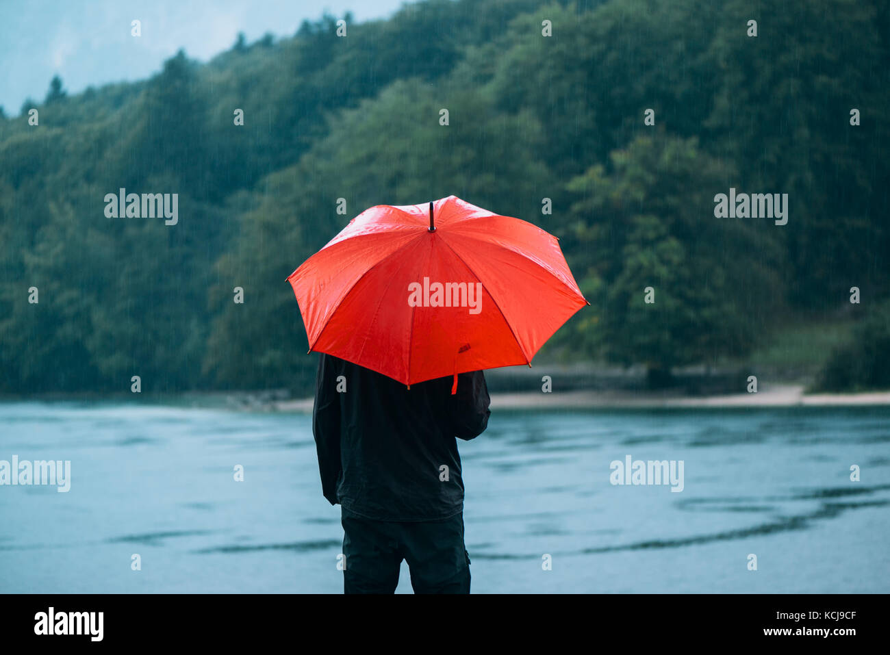 Homme avec parapluie rouge prévoit de la pluie en face d'un lac. triste et solitaire à la personne de sexe masculin dans la distance. Banque D'Images