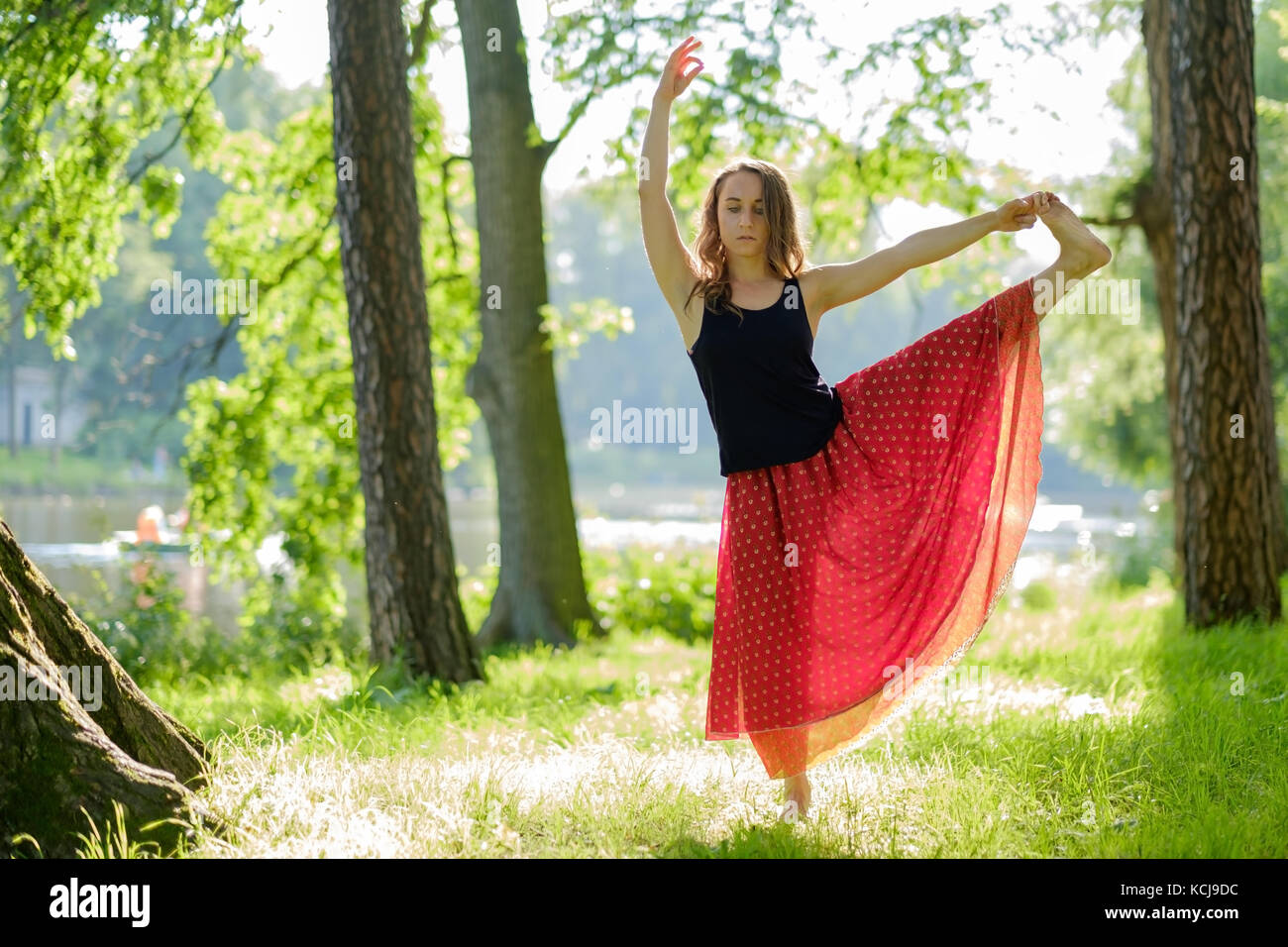 Caucasian woman en jupe rouge faisant équilibre yoga asana dans parc d'été. Banque D'Images