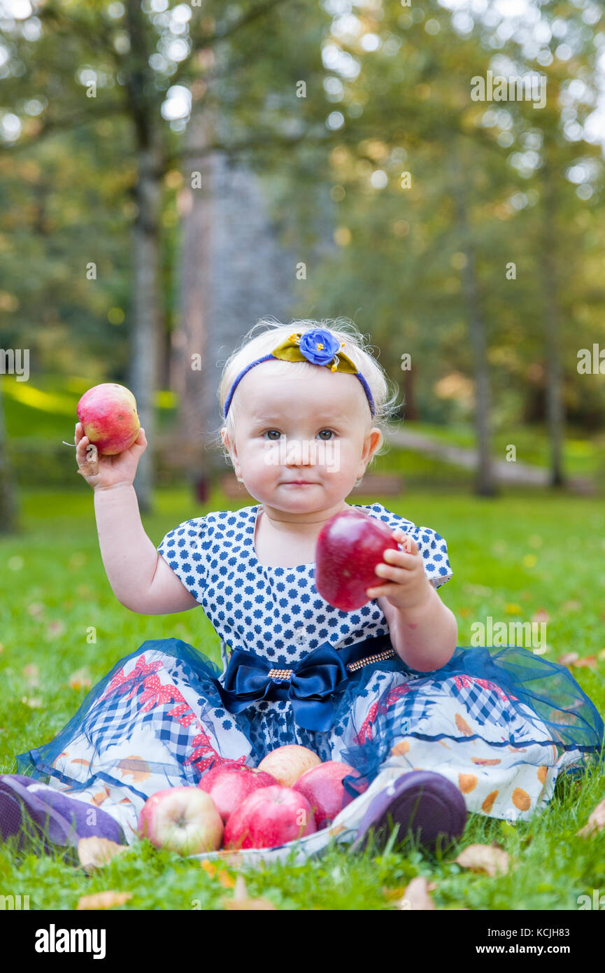 Baby Girl sitting on the grass et de jouer avec ses pommes Banque D'Images