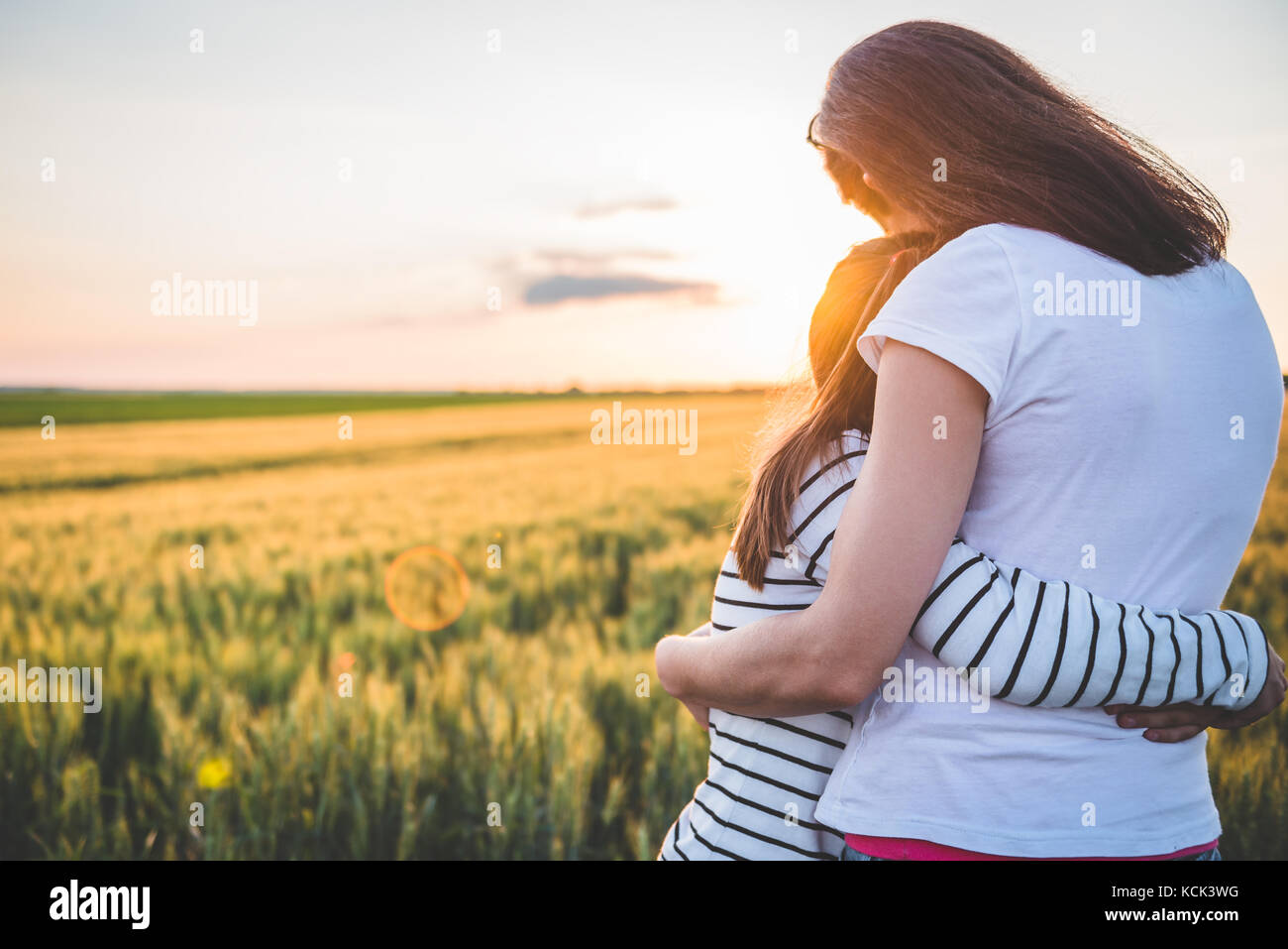 Mother and Daughter hugging au champ de blé pendant le coucher du soleil Banque D'Images