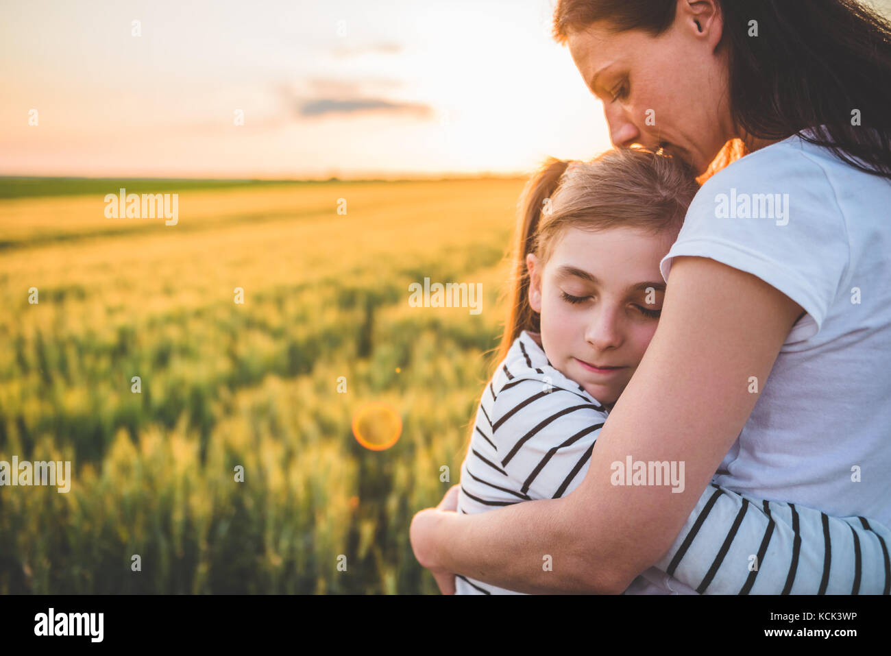 Mother and Daughter hugging au champ de blé pendant le coucher du soleil Banque D'Images
