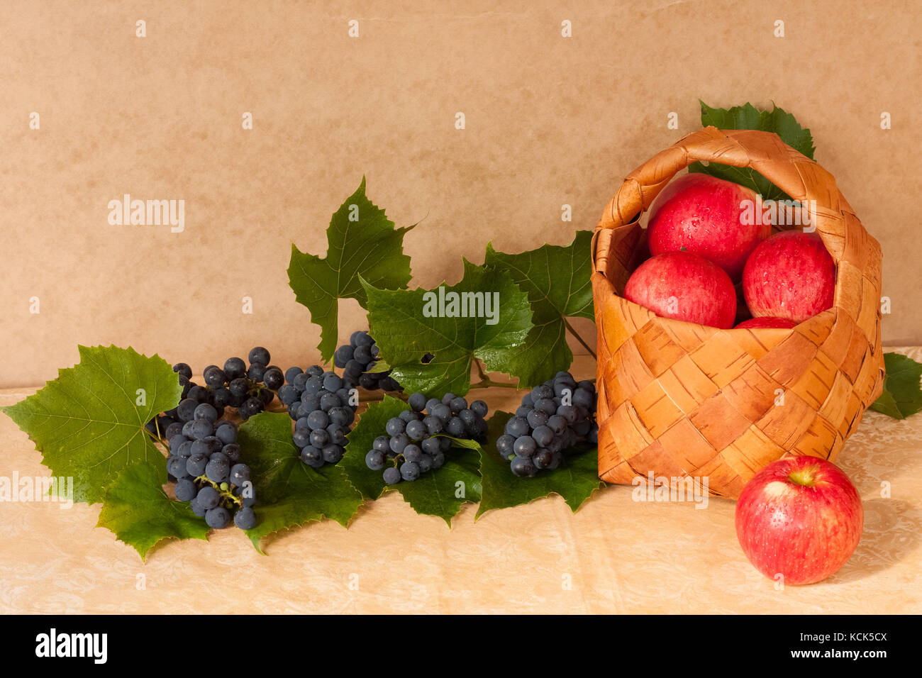 Alimentation saine. fresh fruits mûrs pommes rouges dans panier en osier avec des feuilles et des raisins sur table close up. Banque D'Images