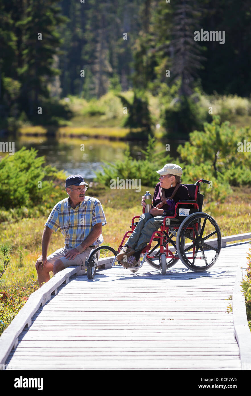 Une femme handicapé et son retner se détendent sur une promenade tout en appréciant une sortie à Paradise Meadows près de Mt. Washington. Mt. Washington, la vallée de Comox, île de Vancouver, Colombie-Britannique, Canada Banque D'Images