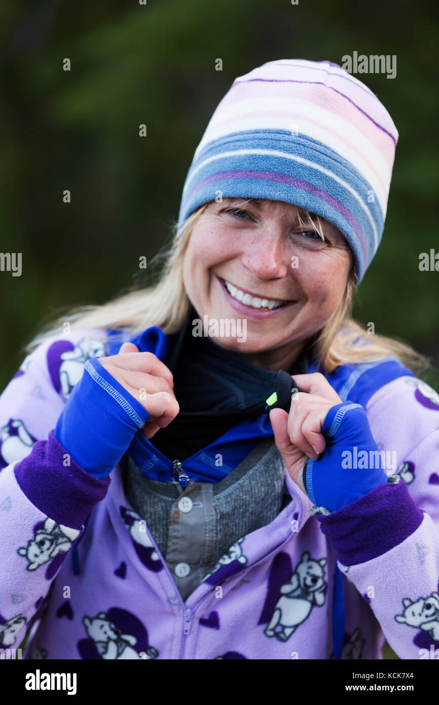 Une femme habillée de couleurs vives camping-partage un rire alors qu'elle décrit ses nombreuses couches de vêtements d'extérieur tout en camping au lac bedwell, parc Strathcona, centre de l'île de Vancouver, Colombie-Britannique, Canada Banque D'Images