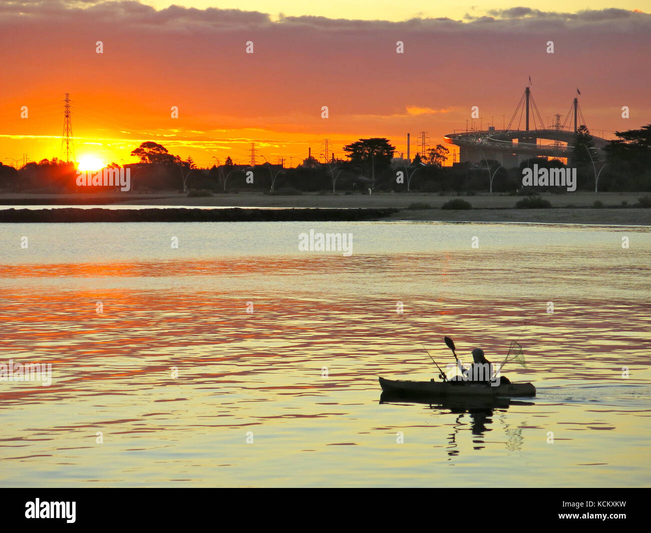 Pêche en canoë au coucher du soleil avec Port Melbourne au-delà et silhouette du pont Westgate à droite. Melbourne, Victoria, Australie Banque D'Images