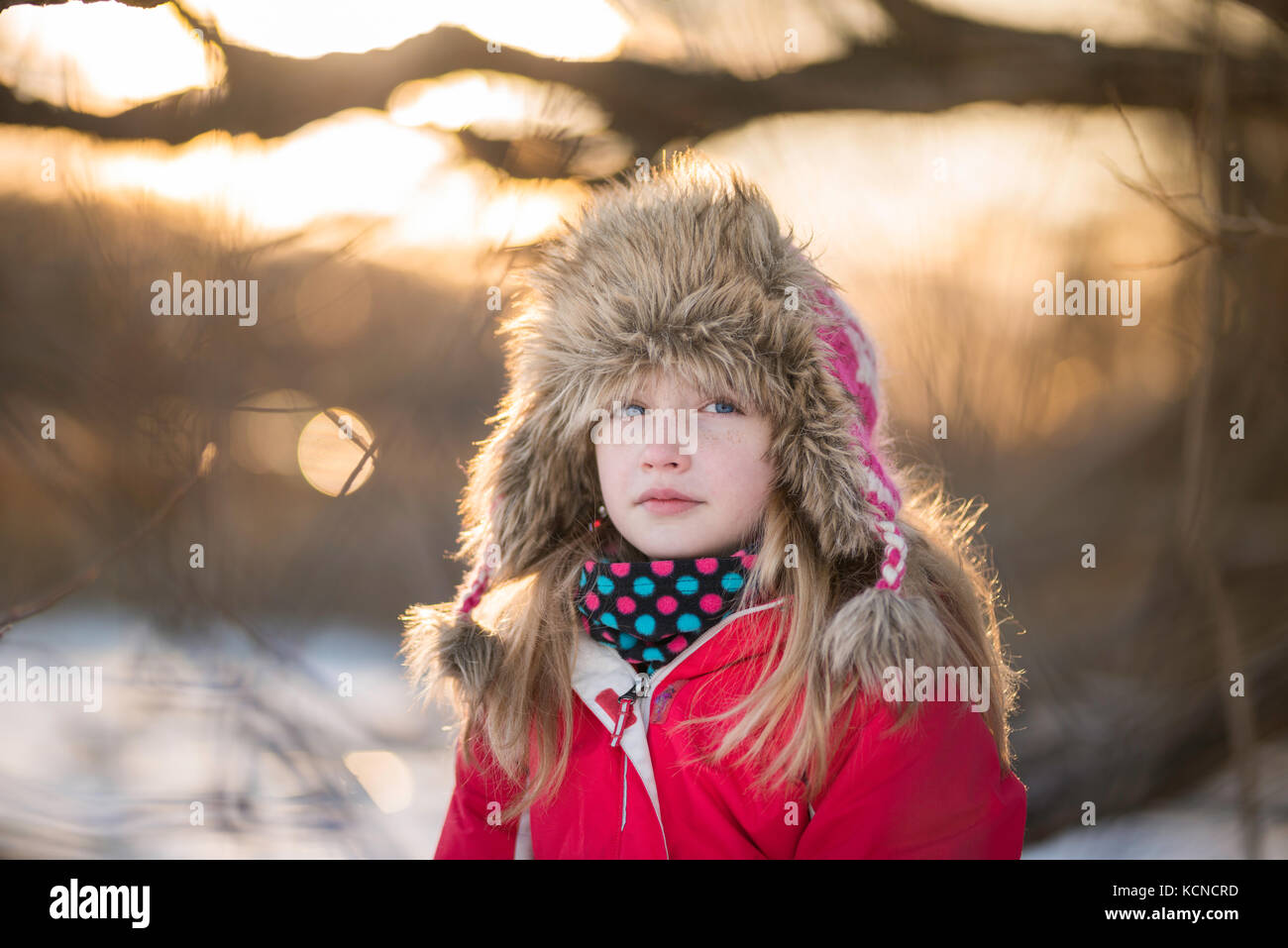 Girl (10) assis dans un arbre sur la rive d'un lac gelé en hiver. Banque D'Images