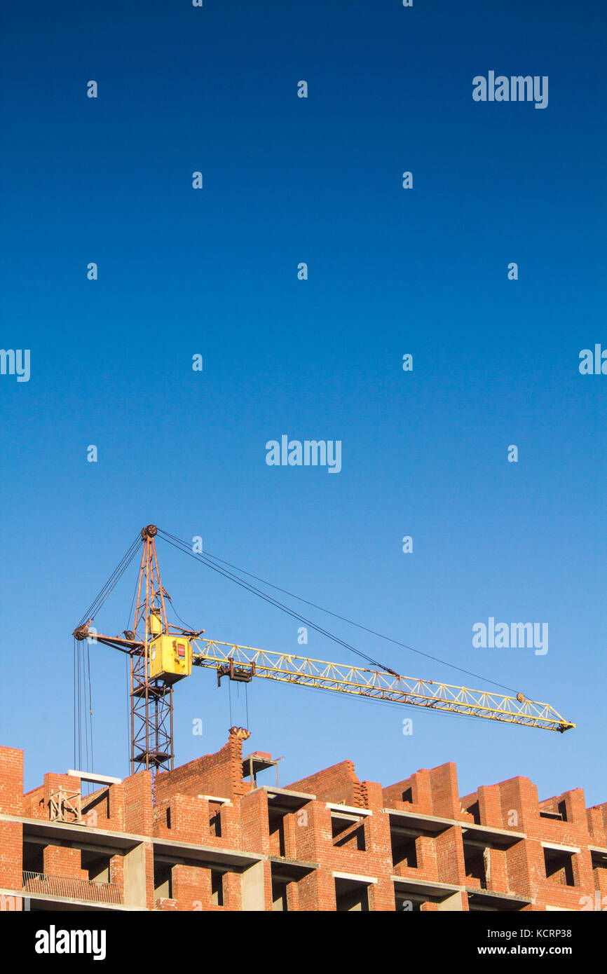 Une grue jaune construit un immeuble de brique rouge Banque D'Images