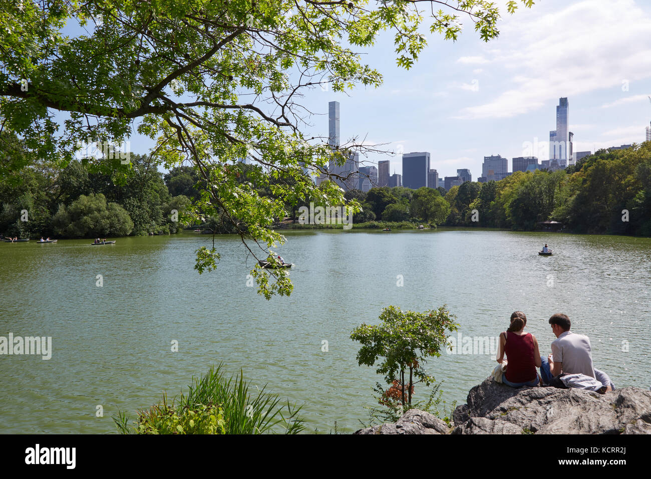 Des gens assis sur les rochers près de l'étang dans Central Park avec vue sur la ville de New York Banque D'Images