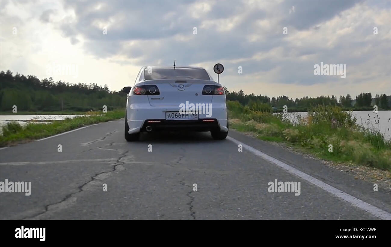 Gros plan sur les roues sport. La scène derrière comme le soleil se couchant avec des éoliennes à l'arrière. voiture de sport blanche sur la route. Vitesse. Voiture roulant sur route. voiture de sport blanche près de la rivière Banque D'Images