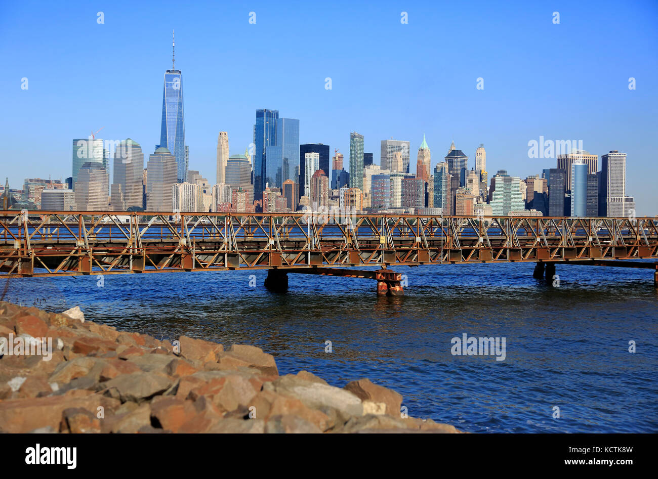 La ligne d'horizon du quartier financier de Lower Manhattan avec un pont à pied relie Ellis Island et Liberty State Park au-dessus de l'Hudson River en premier plan, NJ, USA Banque D'Images