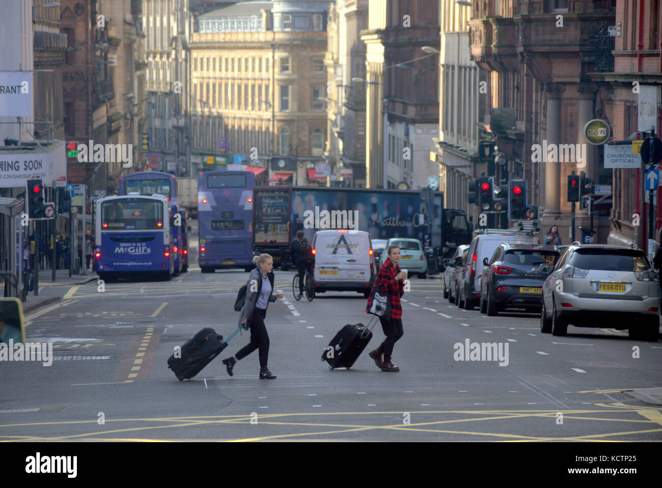Les touristes avec trolley sacs cas traversant la rue occupée de la circulation et de la pollution Union Street, Glasgow, Royaume-Uni Banque D'Images