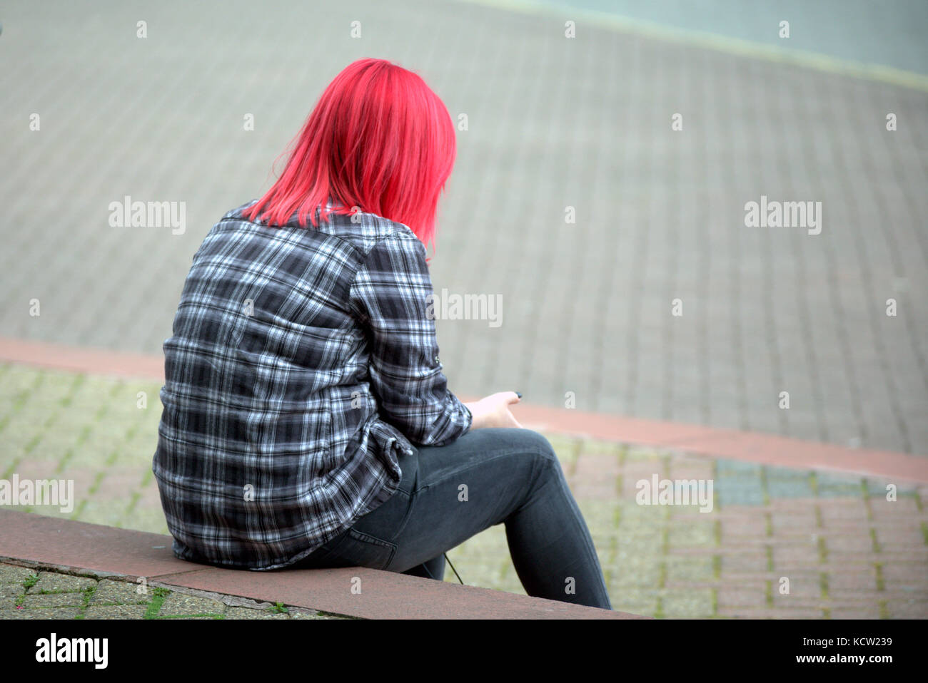 Les cheveux teints en rouge femme fille ado seul assis sur les marches à l'aide de smart mobile phone Banque D'Images