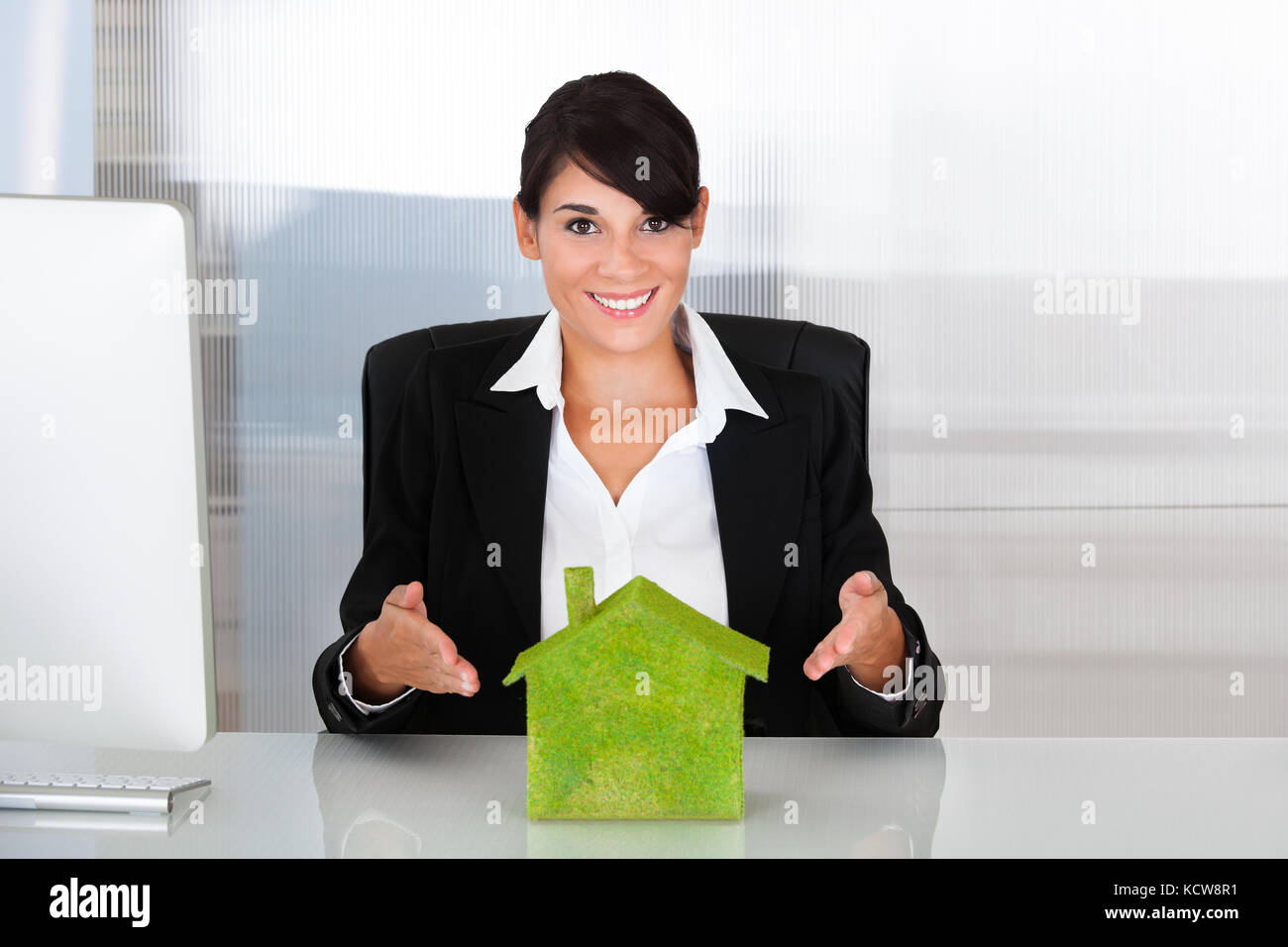 Happy businesswoman holding green eco house at desk Banque D'Images