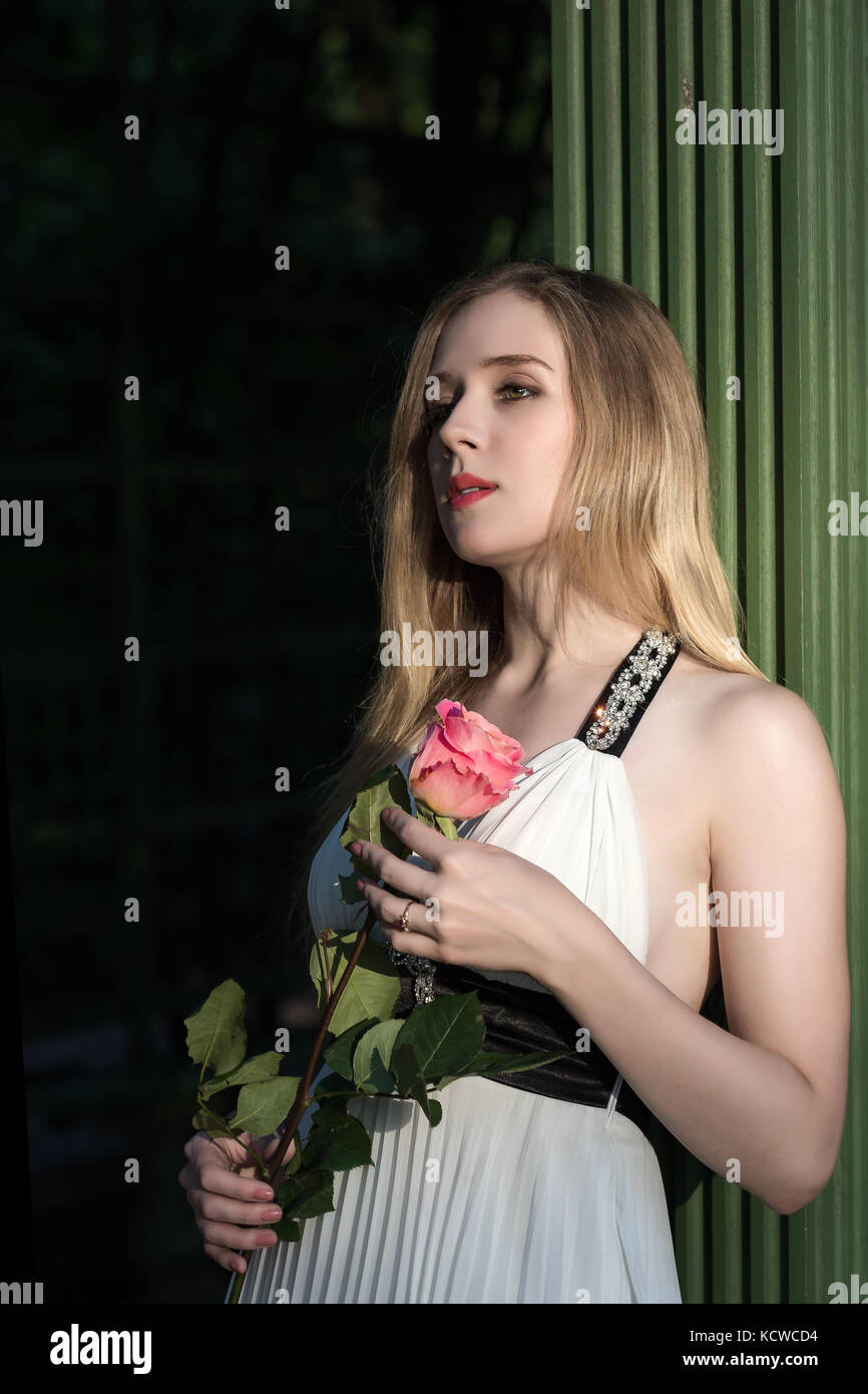 Une fille avec de longs cheveux et une robe blanche avec une rose dans ses mains Banque D'Images