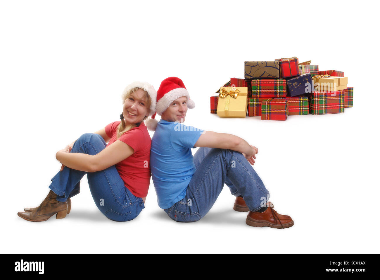 Young happy couple wearing red santa hats sitting on floor dos à dos avec pile de cadeau de Noël dans l'arrière-plan Banque D'Images