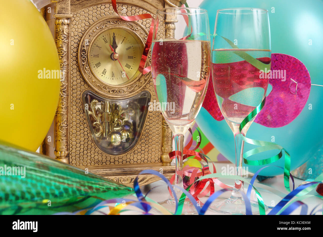 Horloge de table montrant presque minuit, banderoles, ballons, et deux verres de champagne Banque D'Images