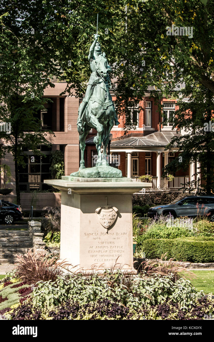 Statue en bronze de sancta joanna d arc - Jeanne d'arc se dresse comme un monument de guerre dans un jardin coloré, un jour ensoleillé Banque D'Images