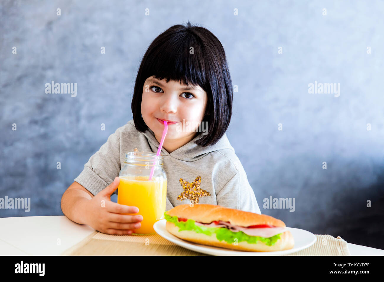 Cute little girl cheveux noir de prendre le petit déjeuner et boire le jus d'orange à la maison Banque D'Images