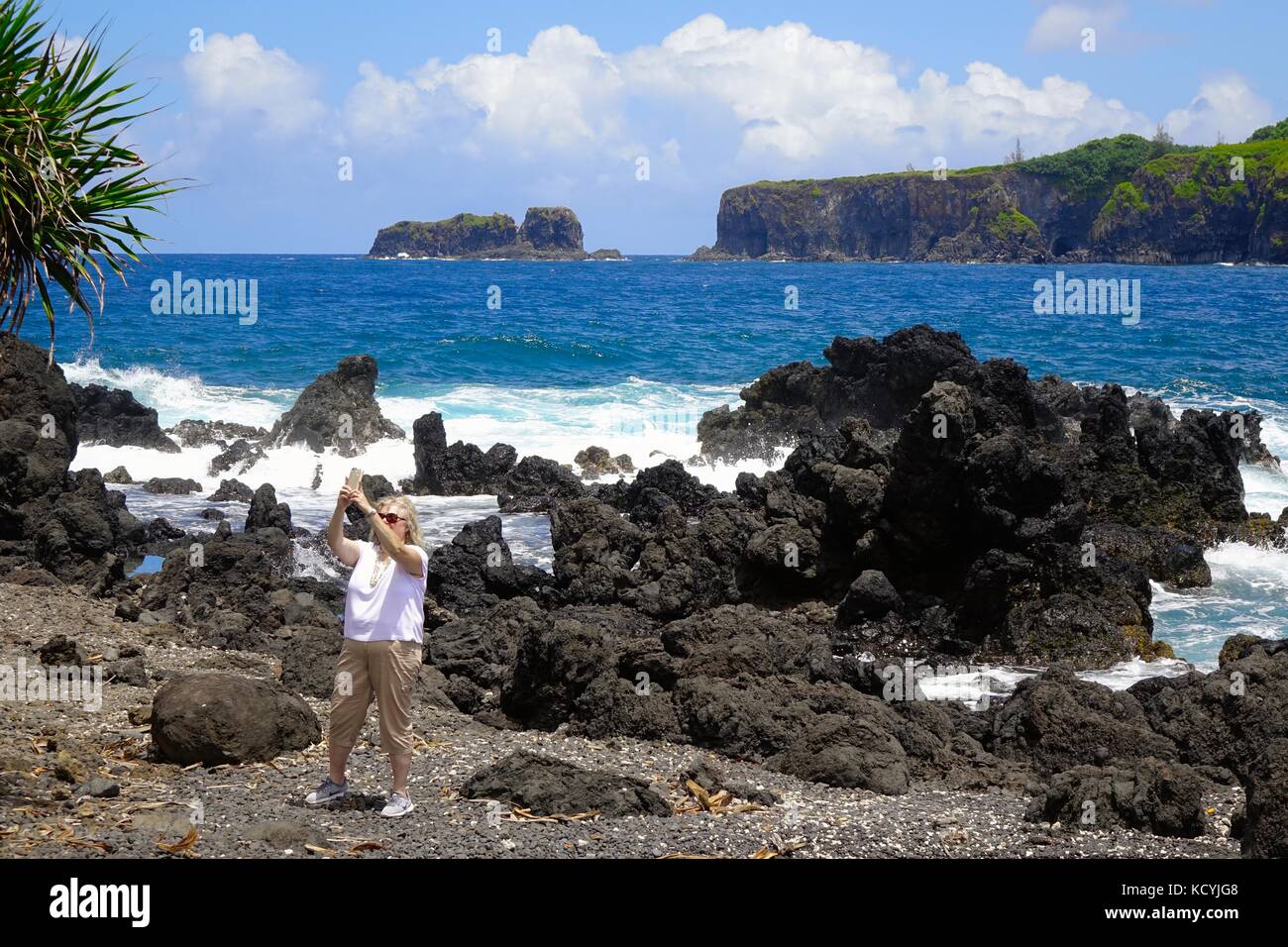 Une femme prend un à la péninsule selfies Keanae comme des vagues s'écraser sur des roches de lave sur la côte Banque D'Images