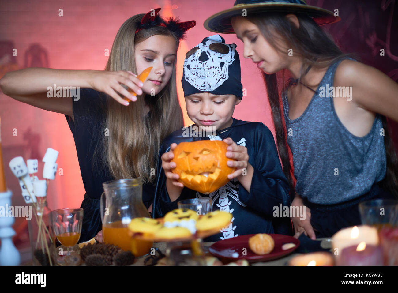 Portrait de trois professionnels enfants vêtus de costumes de Halloween, deux filles et un garçon tenant à la citrouille sculptée en elle pendant party dans décoré ro Banque D'Images