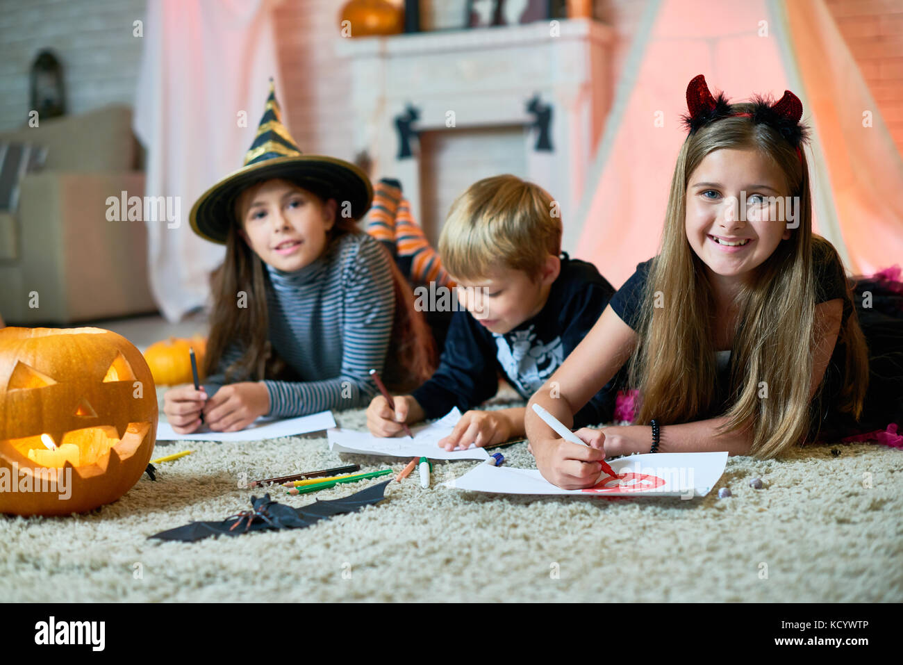 Portrait de groupe de joyeux enfants vêtus de costumes de Halloween réunis au salon confortable décoré pour l'Halloween et de dessin pict colorés Banque D'Images