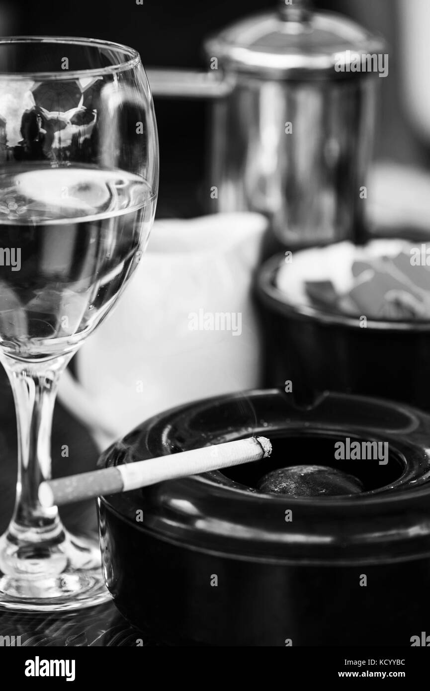 Le noir et blanc des images monochromes d'un verre de vin blanc avec un cendrier et allume sur une table dans un café ou restaurant Banque D'Images