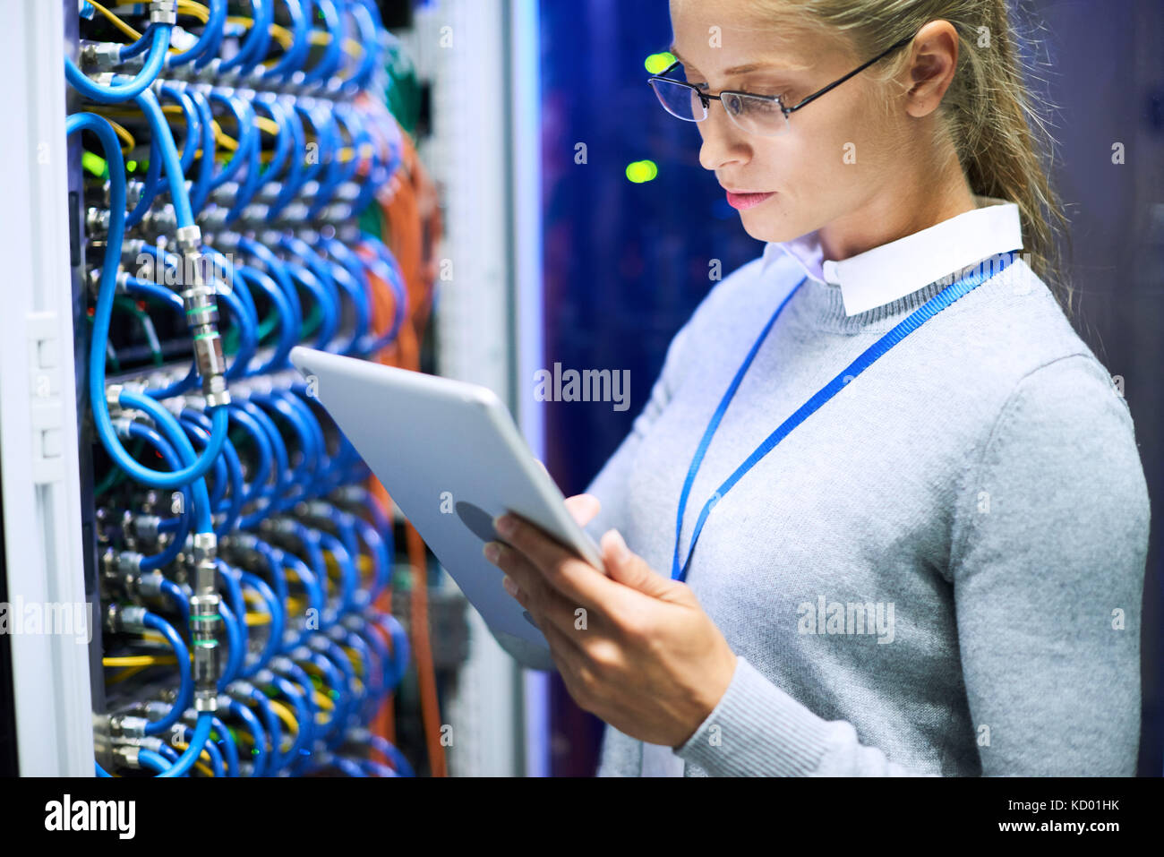 Portrait de femme ingénieur réseau portant des lunettes à l'aide de tablette numérique l'article contre les cabinets de serveurs dans le centre de données Banque D'Images