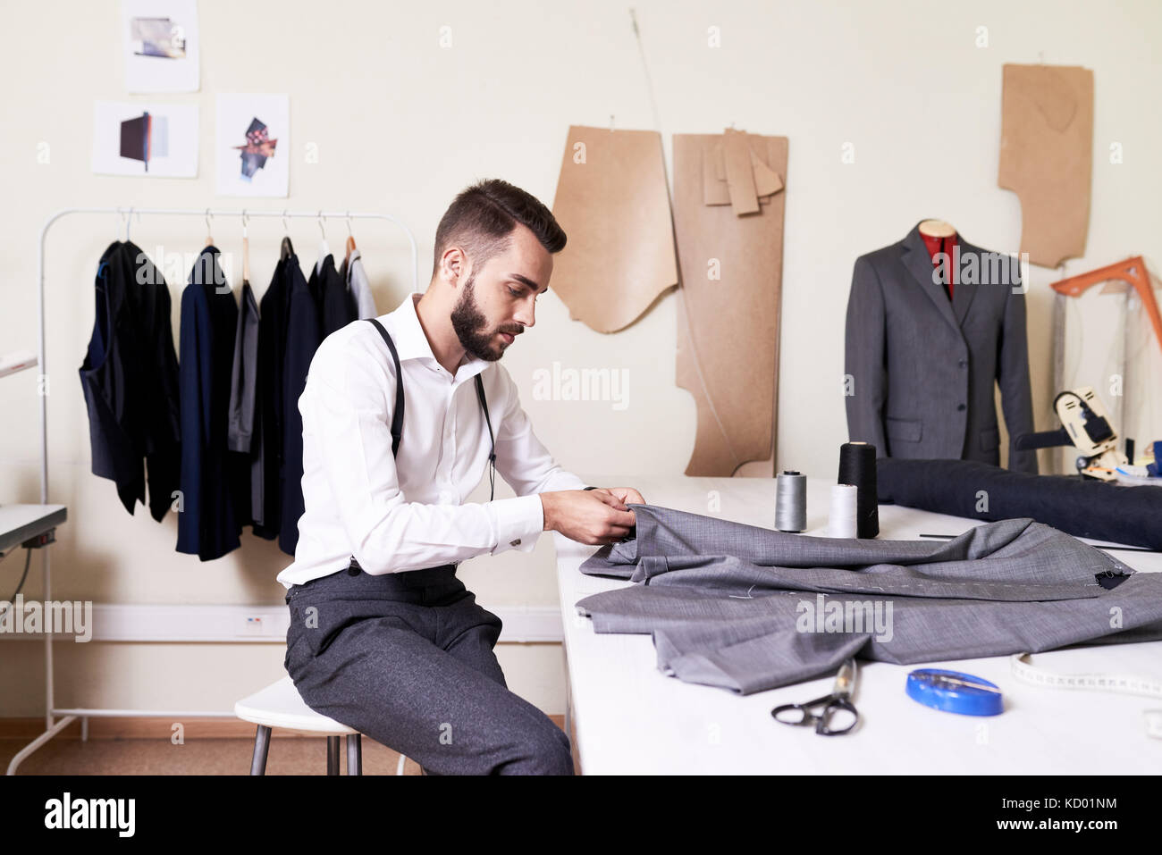 Vue de côté portrait de beau jeune homme costume sur mesure couture à table dans un atelier Banque D'Images