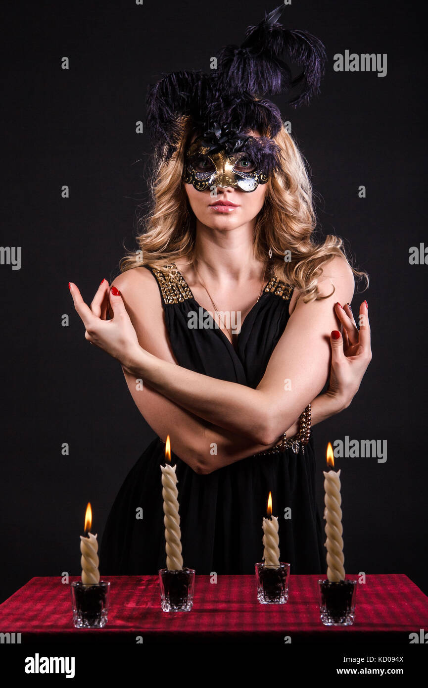 Mystérieuse femme dans un masque près de la table avec des bougies allumée sur fond noir Banque D'Images