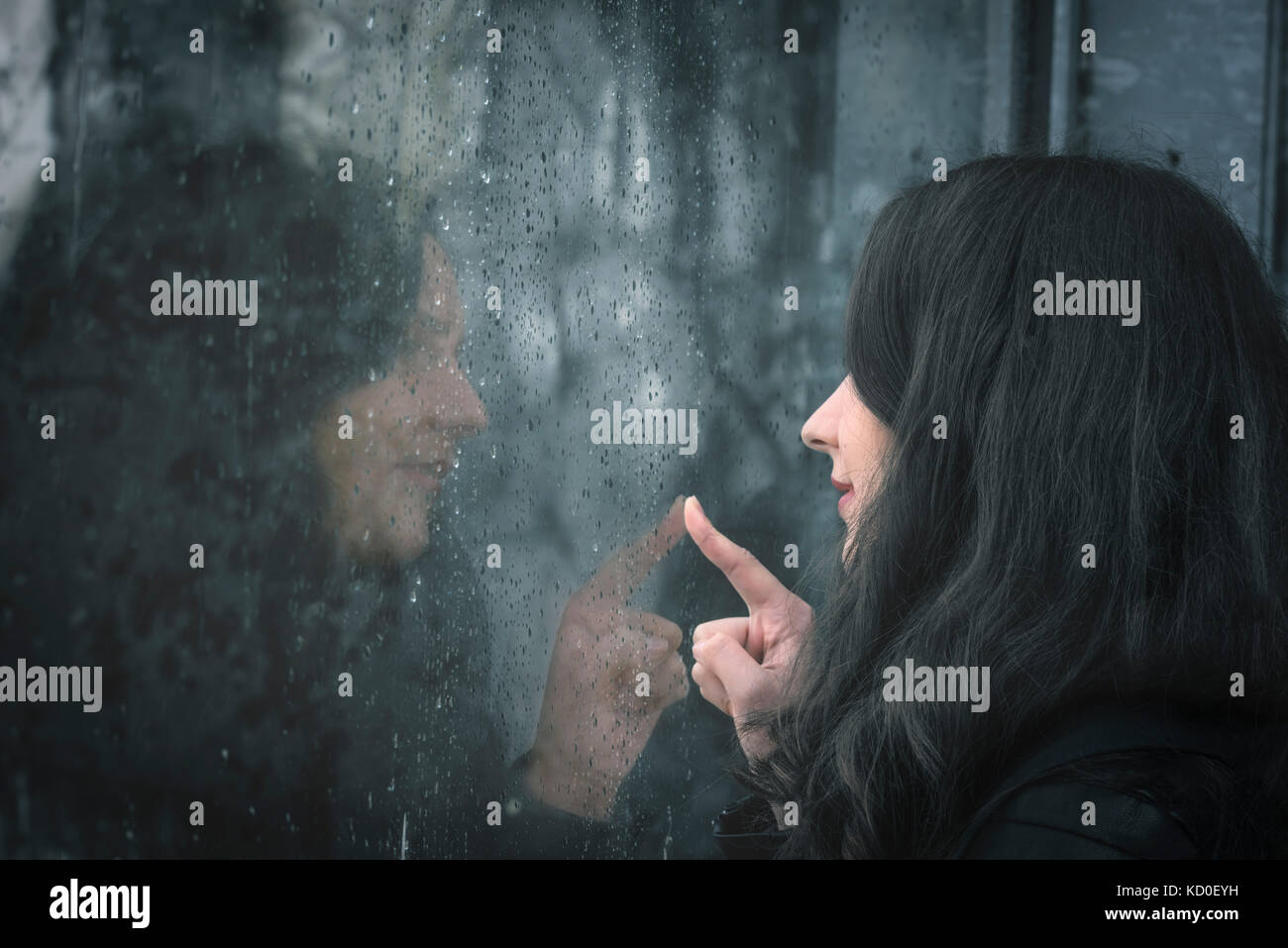 Moody image avec une jeune femme assise en face d'une fenêtre des pluies et touchant avec son doigt Banque D'Images