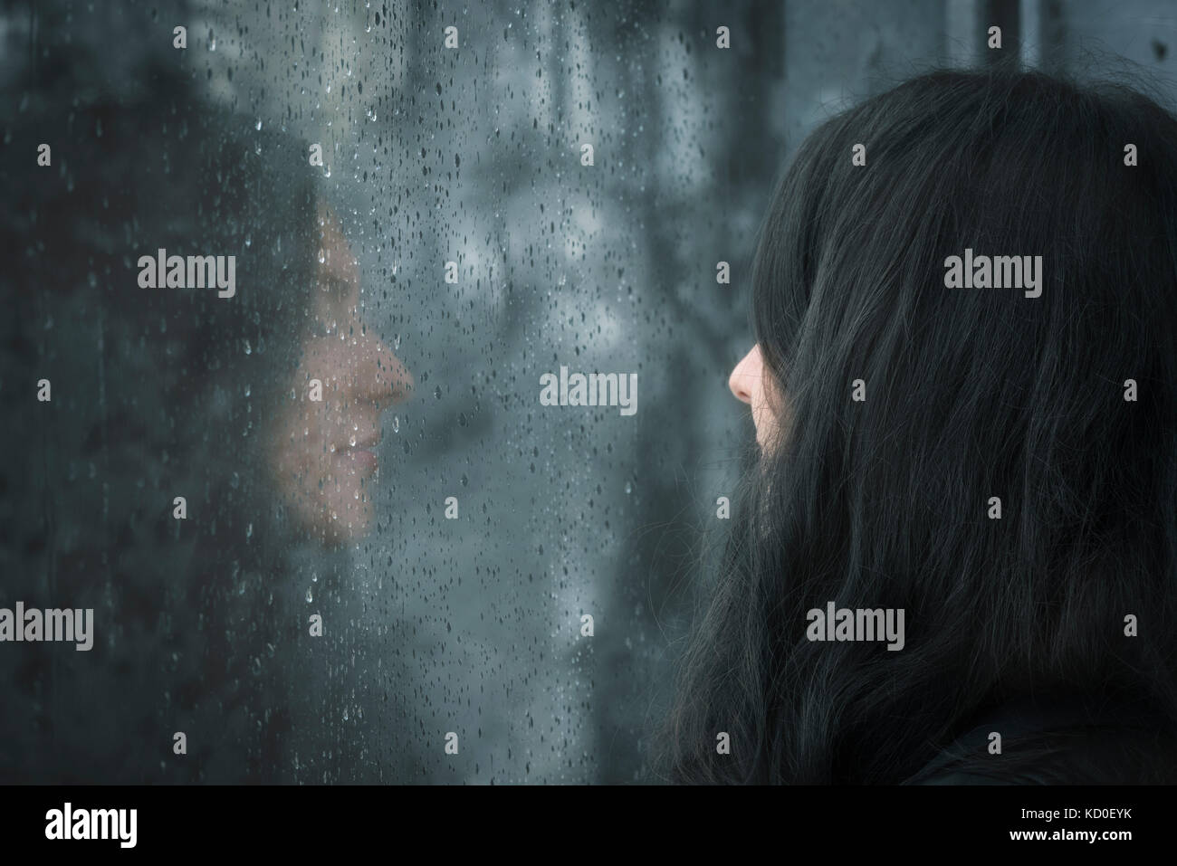 L'image de profil d'une jeune femme brune aux yeux clos penser en face de la fenêtre des pluies Banque D'Images