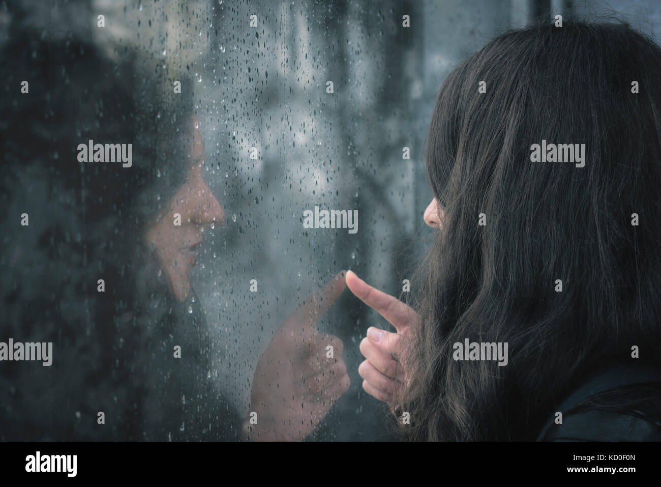 Brunette jeune femme et sa réflexion sur une fenêtre couverte de gouttes de pluie Banque D'Images