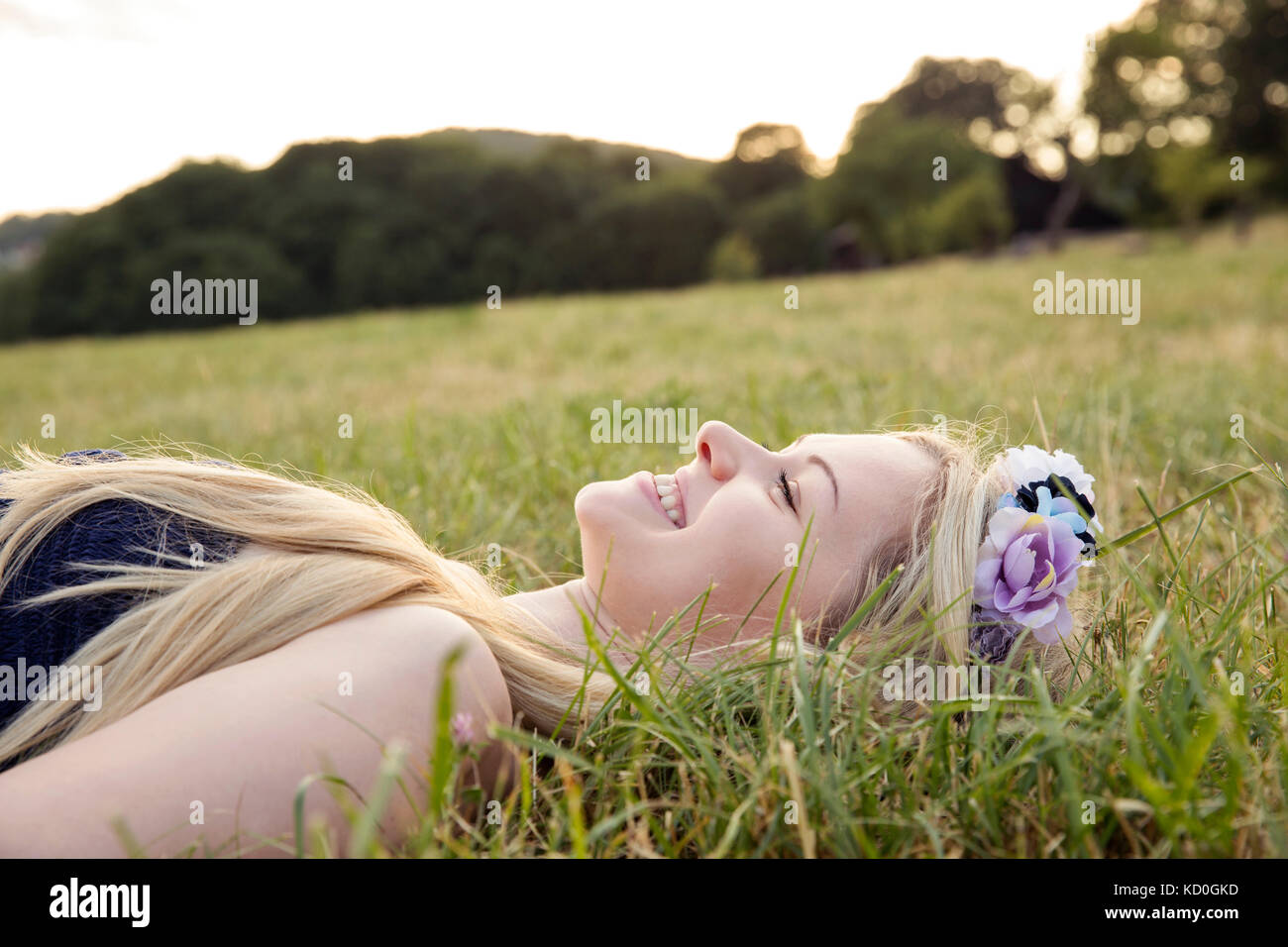 Femme avec des fleurs dans les cheveux lying on grass smiling Banque D'Images