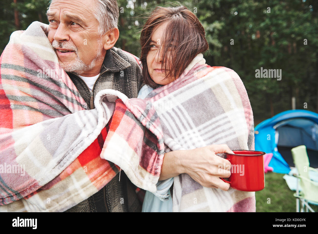 Mature couple debout à côté de la tente, enveloppé dans une couverture Banque D'Images