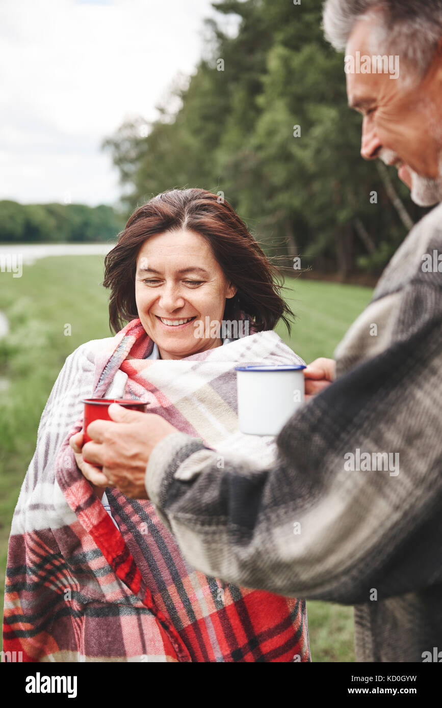 Mature couple standing in rural, holding boisson chaude, woman wrapped in blanket Banque D'Images
