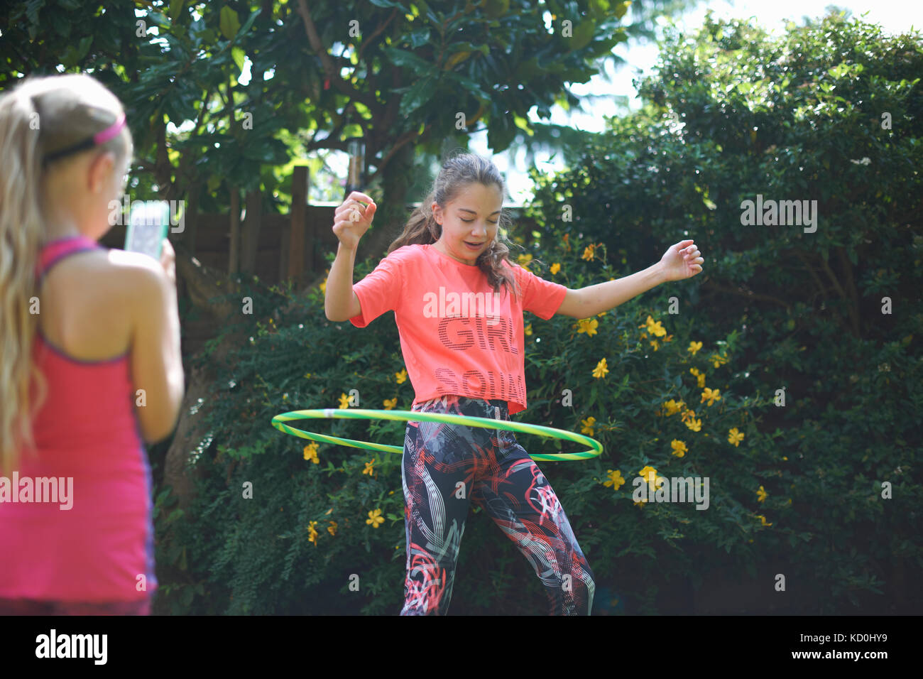 Girl photographing young soeur hoola hoop dans jardin Banque D'Images