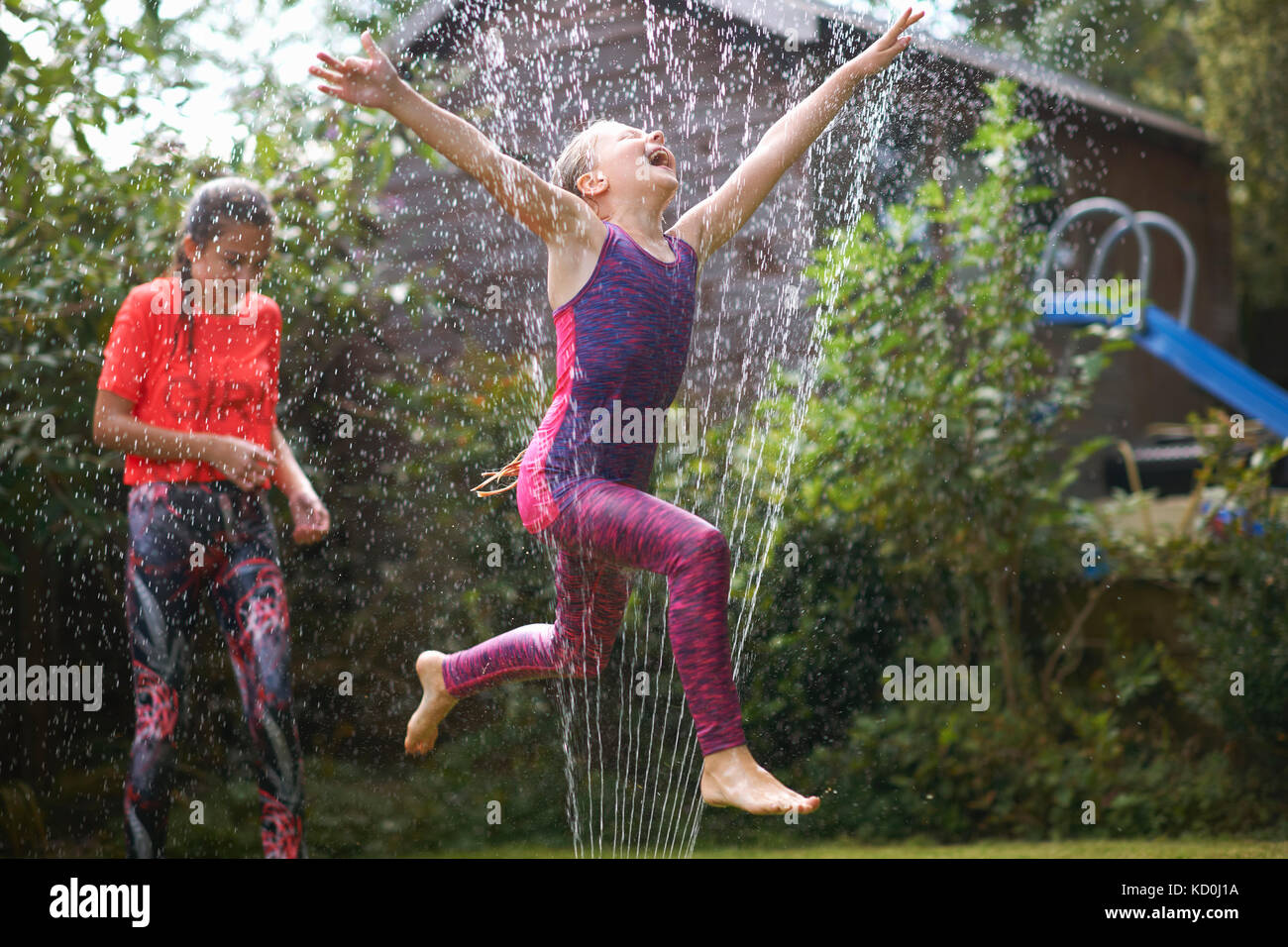 Les filles sautant sprinkleur jardin Banque D'Images