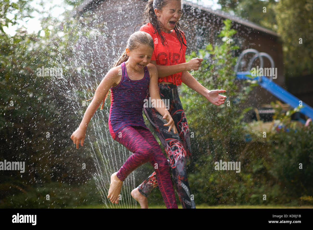 Les filles sautant sprinkleur jardin Banque D'Images