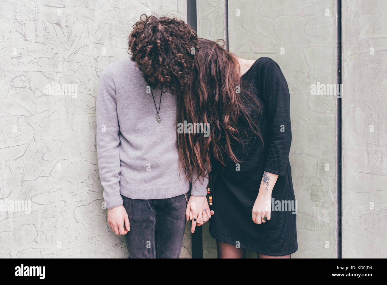 Young couple outdoors, debout contre le mur, tenant les mains, les cheveux couvrant leurs visages, Banque D'Images