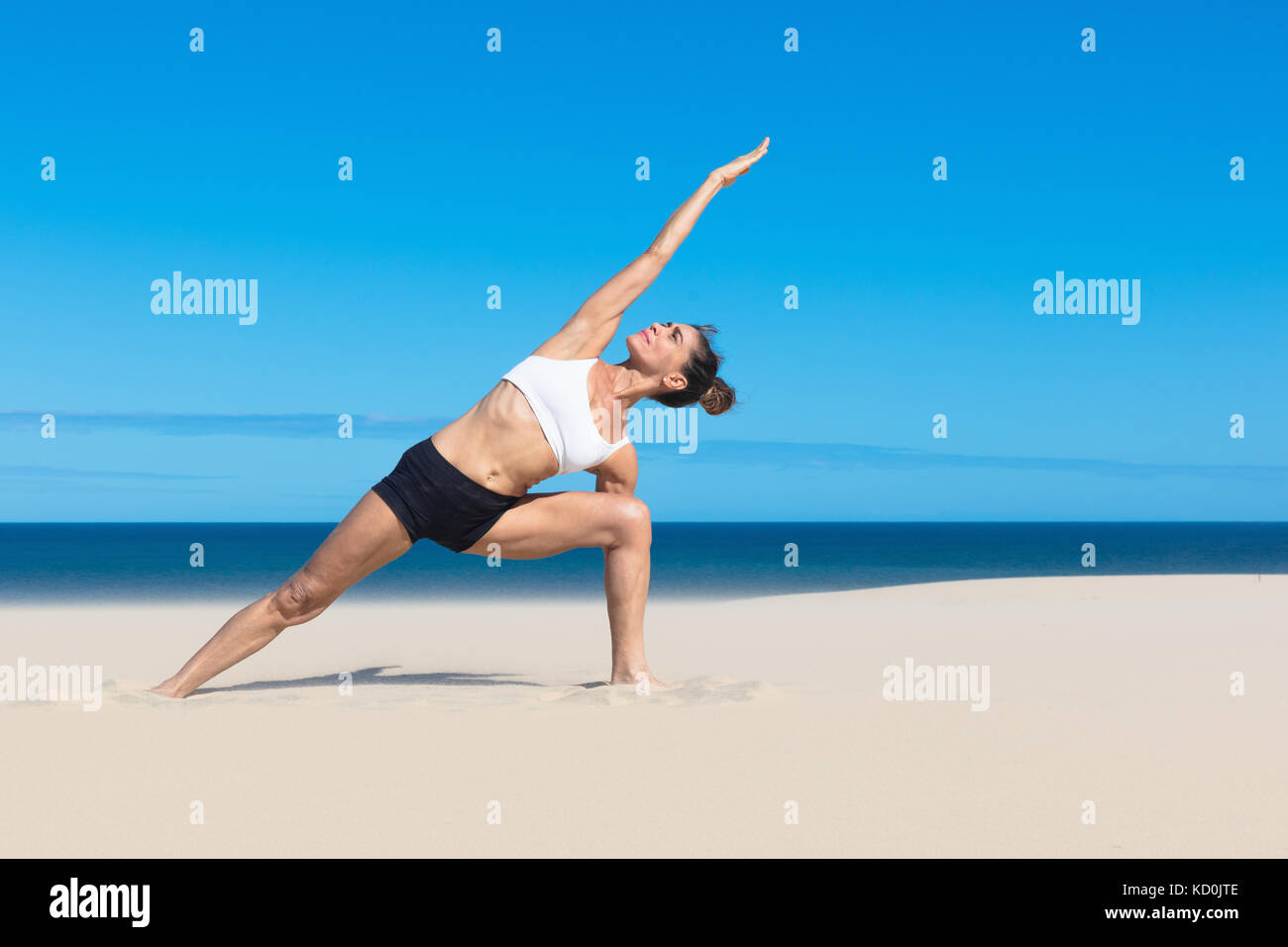 Woman on beach pliant latéralement les bras levés en position de yoga Banque D'Images