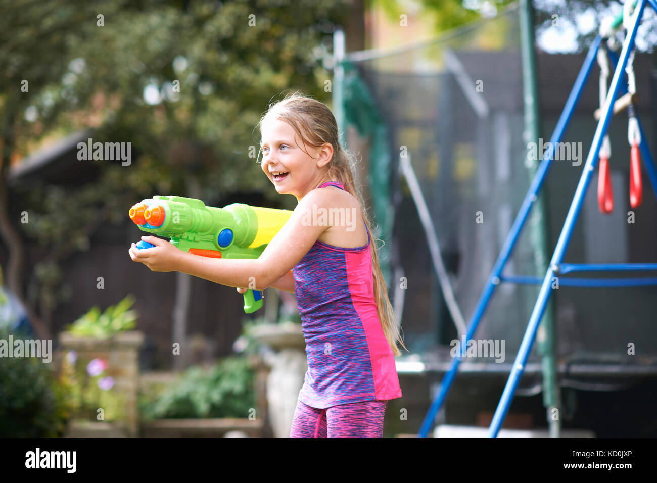 Fille aux cheveux mouillés holding water gun in garden Banque D'Images