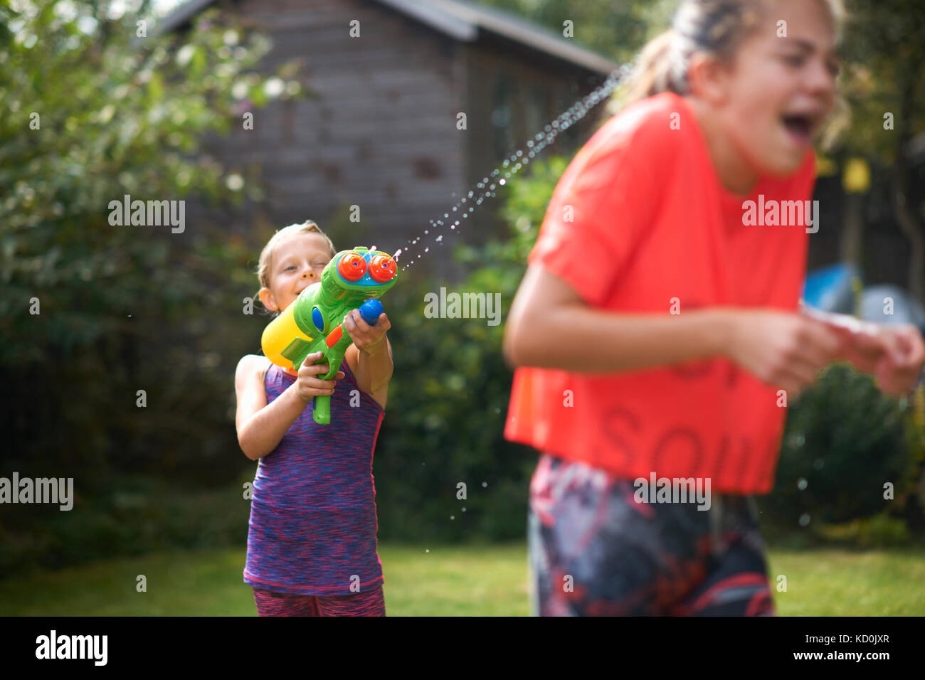 Boy squirting ses sœurs adolescentes avec canon à eau en jardin Banque D'Images