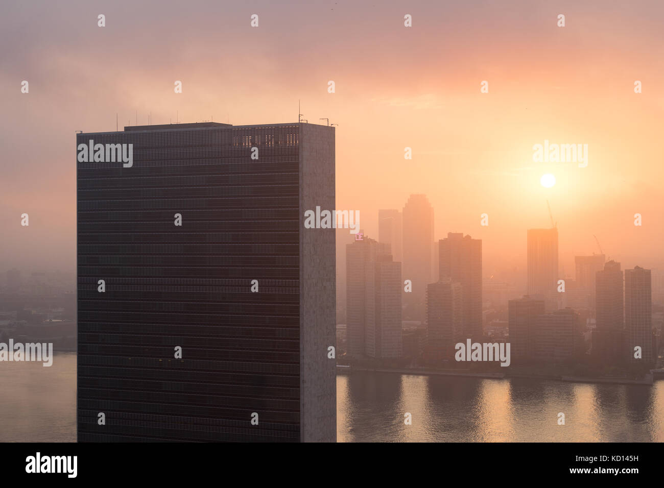 Colorful sunrise ciel derrière un bâtiment du secrétariat de l'ONU. East River et de Long Island City skysrapers dans le brouillard derrière elle. Banque D'Images
