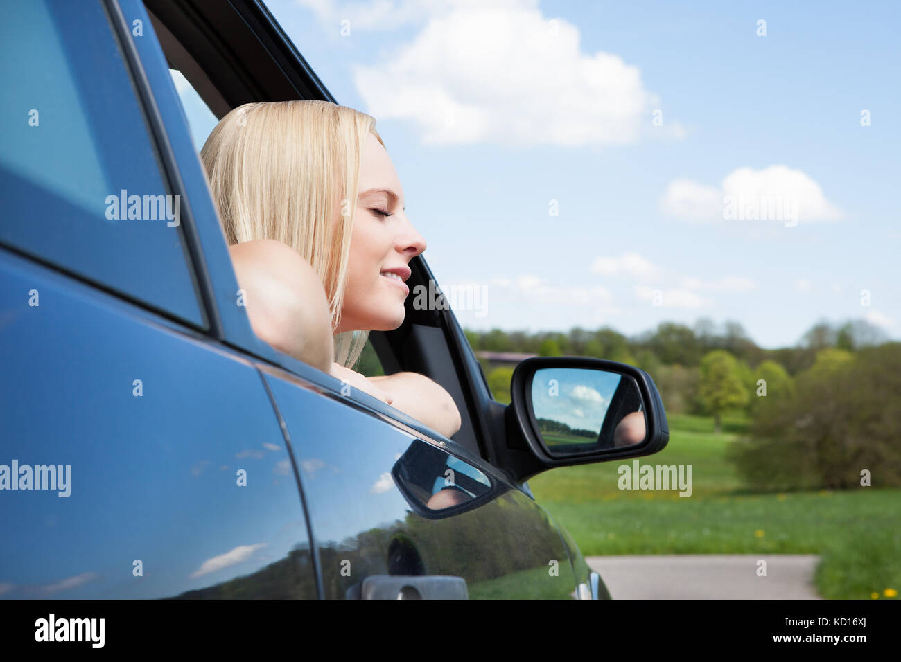Portrait of happy young blonde woman leaning on car window Banque D'Images